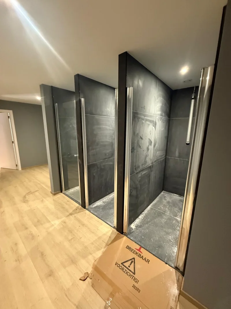 Polvo y restos de obra visibles en las paredes y bases de varias duchas