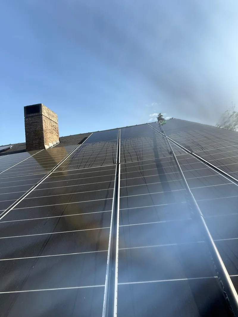 Limpieza de paneles solares en un tejado con cepillo y pértiga