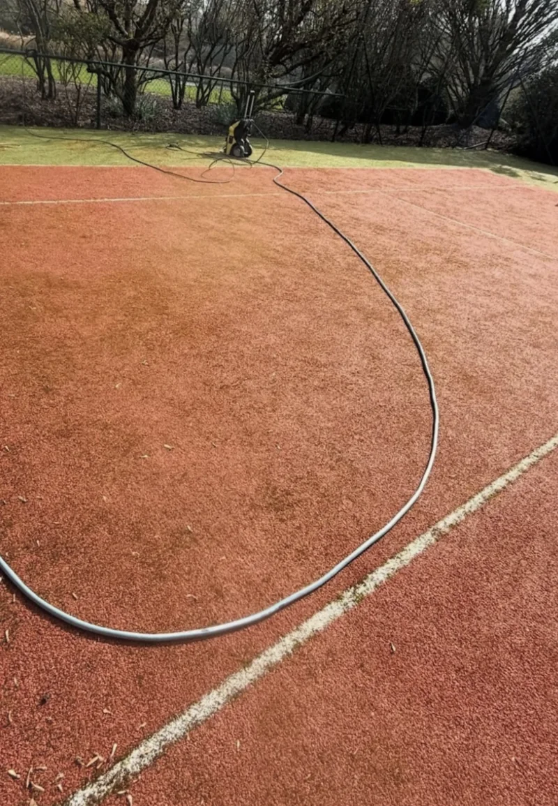 Equipo y manguera durante la limpieza profunda de la pista de tenis